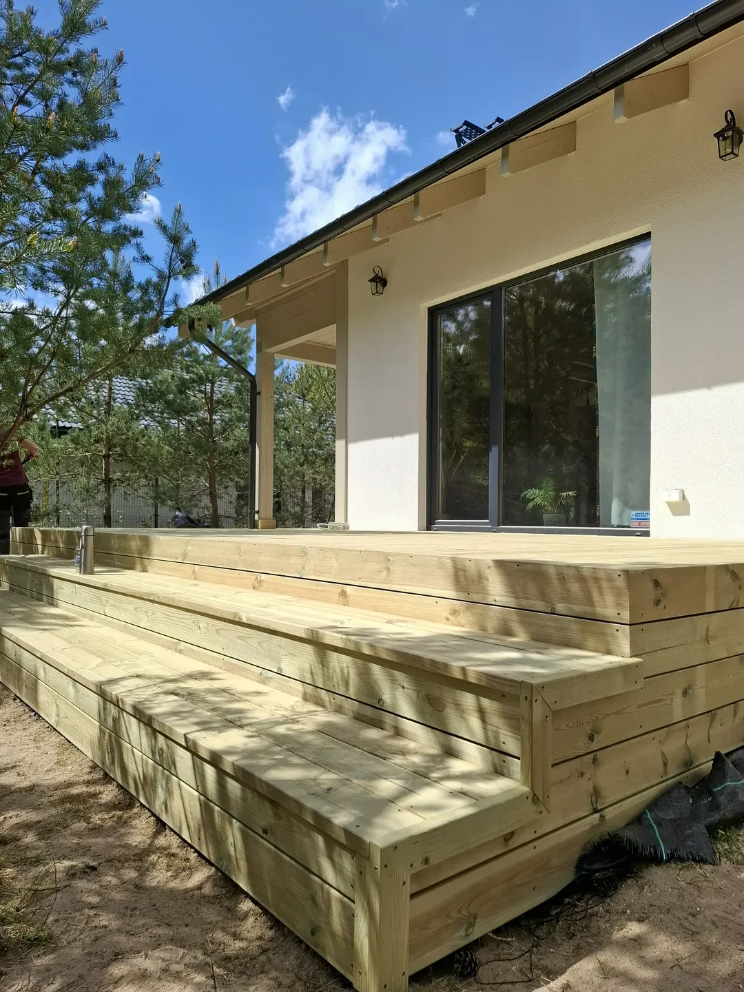 Nowo wykonany drewniany taras z siedziskiem i stopniem przy elewacji budynku