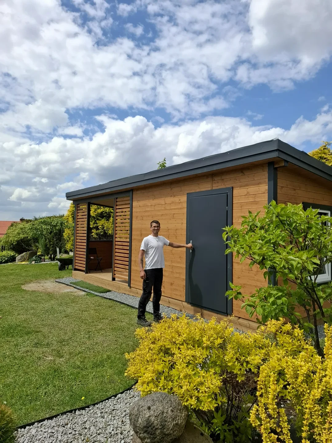 Domki ogrodowe drewniane z ciemnymi drzwiami i tarasem, mężczyzna otwiera drzwi