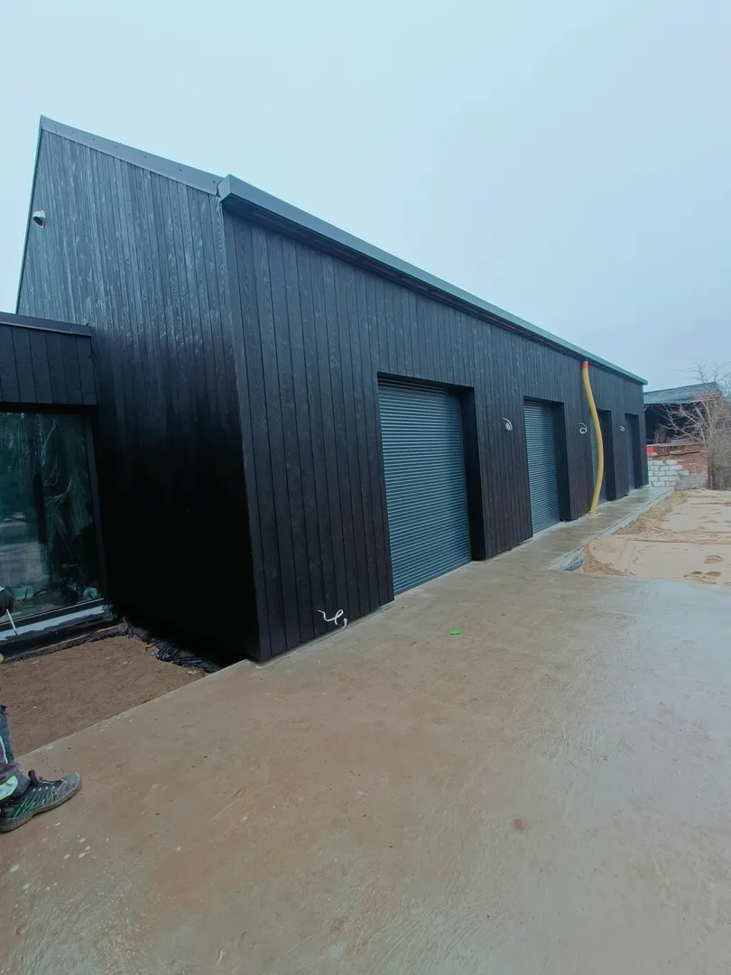 Nowoczesna wiata garażowa z ciemnej drewnianej elewacji i trzema rolowanymi bramami