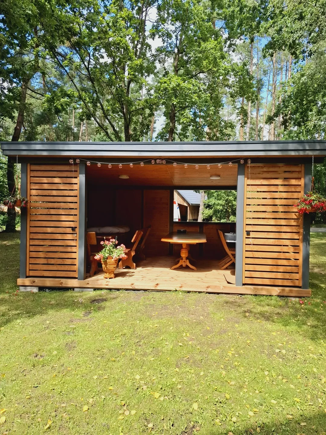 Drewniana altana ogrodowa z otwartą werandą, stołem, ławką i wiszącymi kwiatami