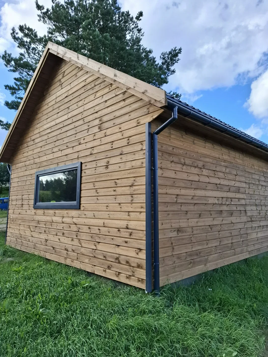 Elewacje drewniane małego domku ogrodowego z czarnym orynnowaniem i pojedynczym oknem