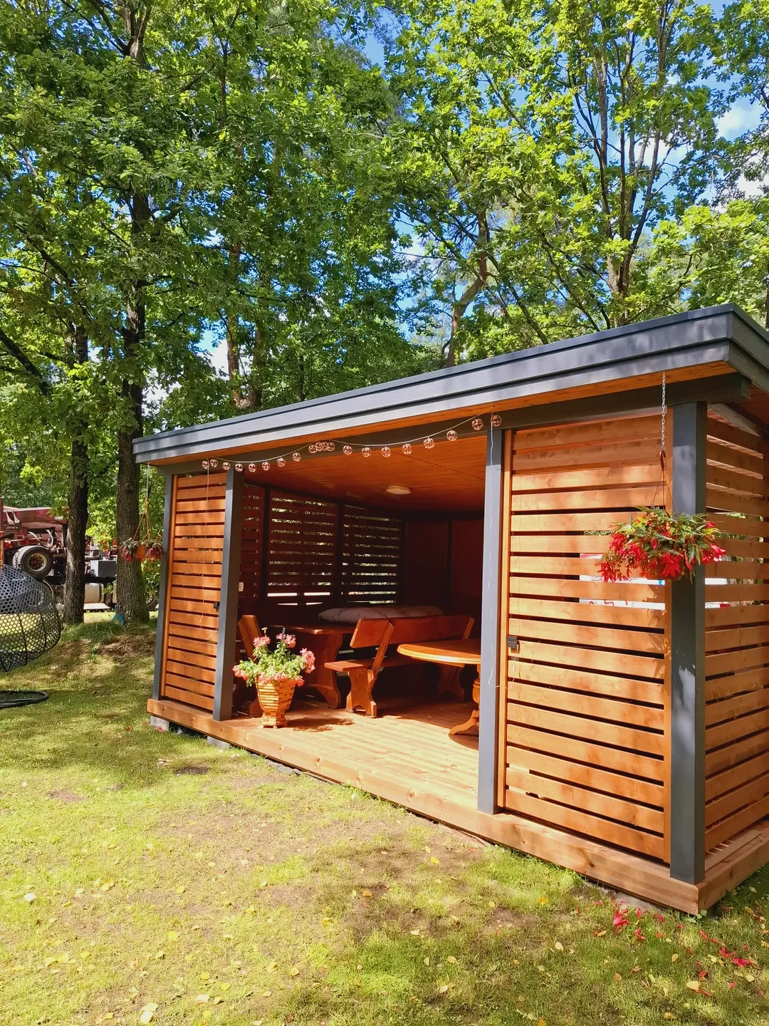 Altany ogrodowe drewniana altana z meblami, doniczkami i oświetleniem na tarasie wśród drzew