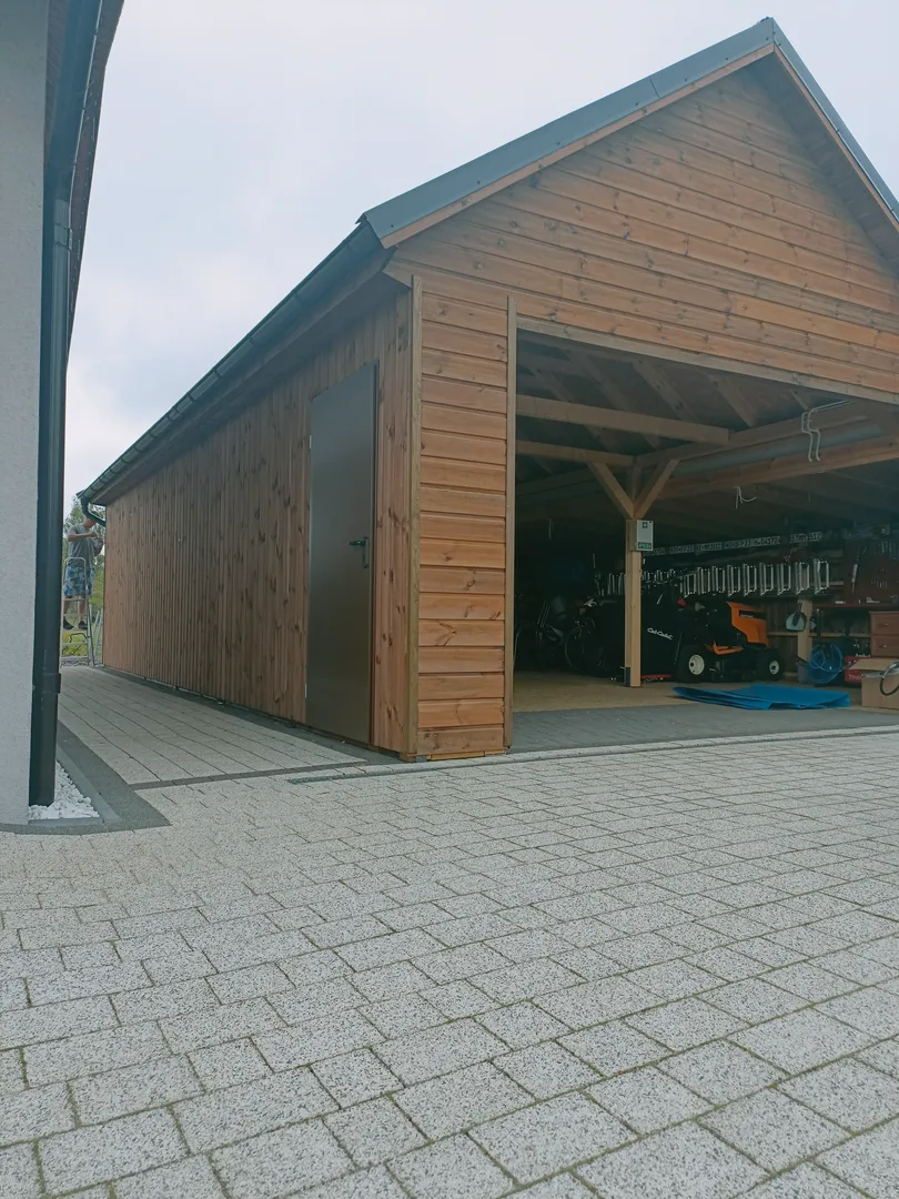 Drewniana wiata garażowa z otwartą konstrukcją i podjazdem z kostki