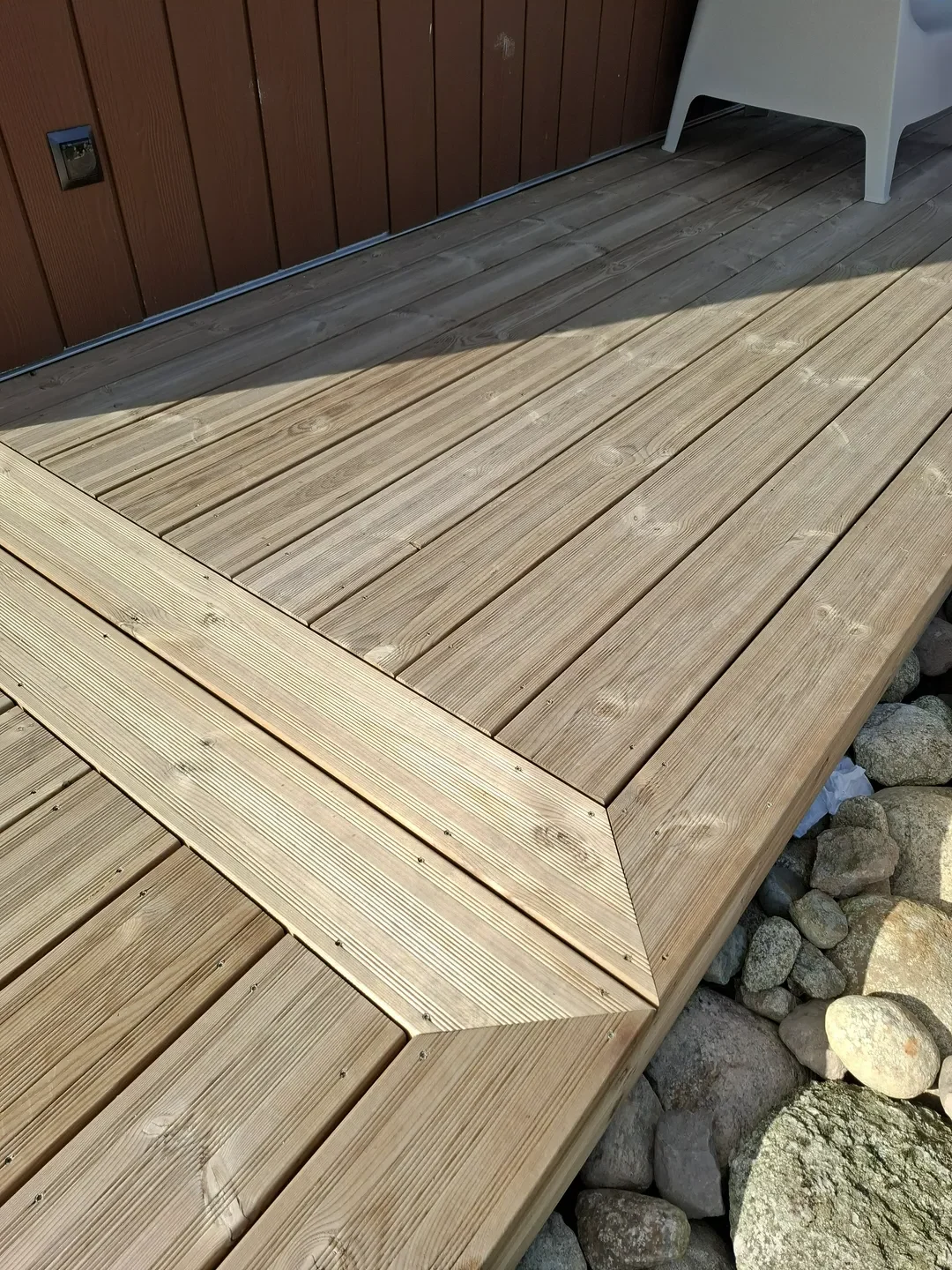 Drewniany taras z listwami ułożonymi w geometryczny wzór przy kamiennej obsadzie