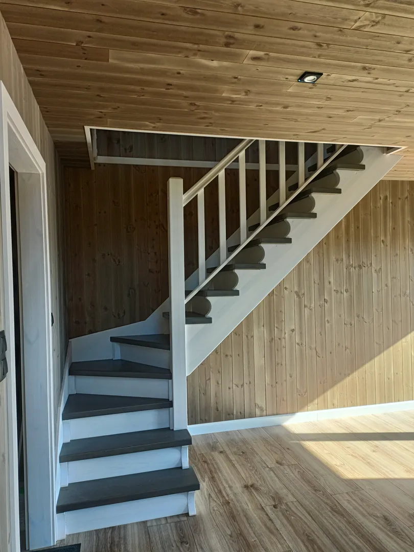 Białe schody drewniane z ciemnymi stopniami we wnętrzu z drewnianą boazerią – wykończenia wnętrz