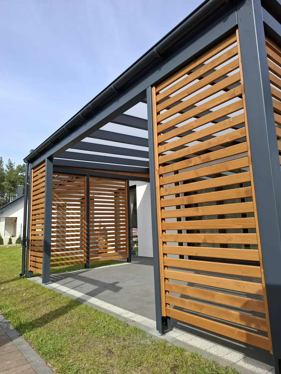 Konstrukcja zadaszenia tarasu z drewnianych lameli i stalowych belek przy ścianie budynku