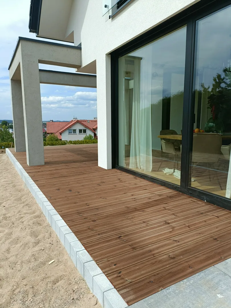 Montaż deski kompozytowej tworzący nowoczesny taras przy dużych przeszkleniach domu