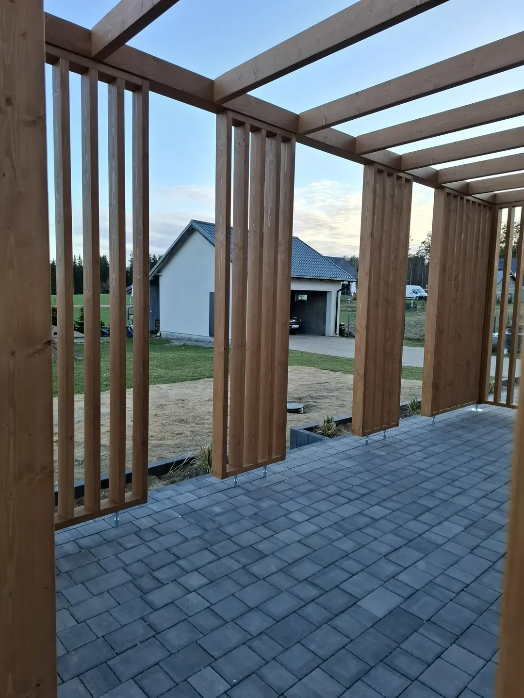 Pergole drewniane na tarasie z kamiennych płytek i drewnianych słupów