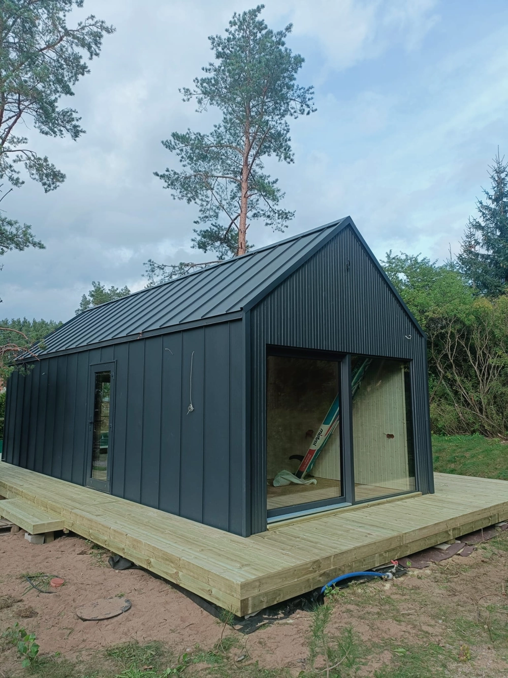 Domki letniskowe drewniane: czarny budynek na drewnianym tarasie z dużymi przeszklonymi drzwiami