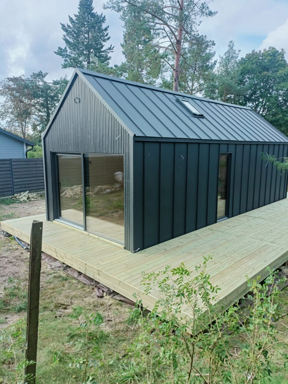 Taras z jasnych drewnianych desek przy nowoczesnym czarnym domku drewnianym