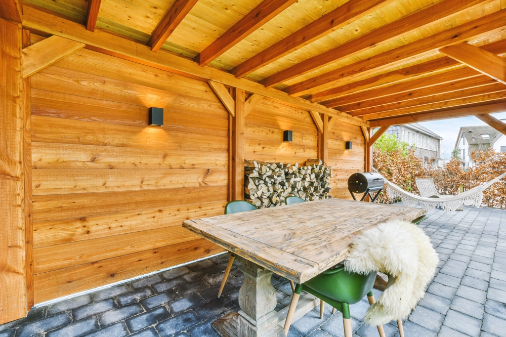 Zadaszenia tarasów: drewniana konstrukcja z dachem nad stołem i krzesłami na patio