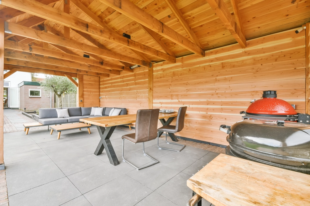 Zadaszenie tarasu z drewnianą konstrukcją, meblami ogrodowymi oraz grillem ceramicznym
