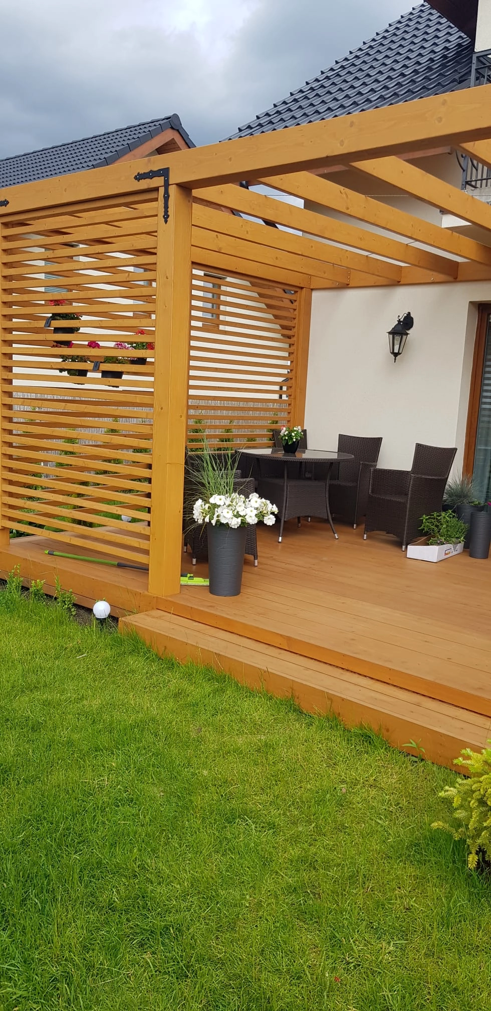 Pergole drewniane: otwarta konstrukcja z poziomymi listwami, taras z kompozytowej deski, meble ogrodowe